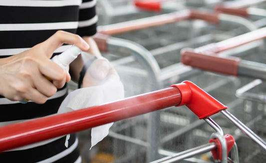 Person Spraying Shopping Cart with Sanitizing Spray