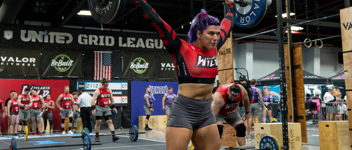 A United Grid League athlete lifting overhead during a GRID match, with the league banner behind
